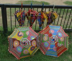 two colorful umbrellas sitting next to each other on the grass near a fence with an iron railing behind them