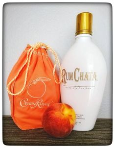 an orange bag next to a bottle of rum chaka and an apple on a table