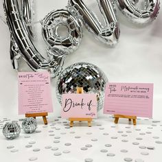 a table topped with lots of silver foil balloons and place cards for guests to write their names