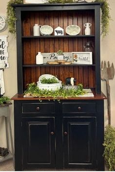 a black china cabinet with greenery on the top and shelves above it in a kitchen