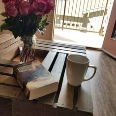 a wooden table topped with books and a vase filled with flowers next to a window