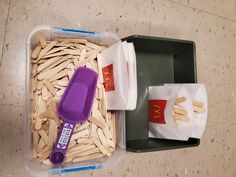 a plastic container filled with hotdogs and fries next to a purple spatula