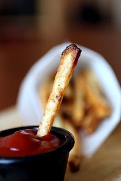 a small black bowl filled with ketchup and french fries on top of a wooden table