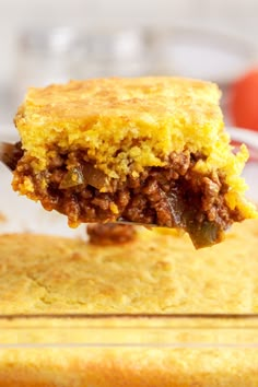 a piece of cornbread casserole being held up by a fork with meat and cheese on it