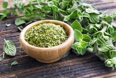 a wooden bowl filled with green herbs on top of a table