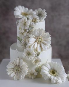 a three tiered cake with white flowers on it's side and the top layer is covered in icing