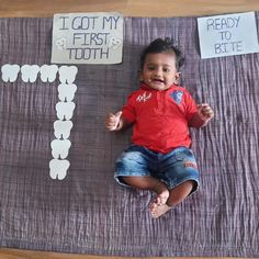 a baby laying on top of a wooden floor next to paper cutouts that say i got my first tooth