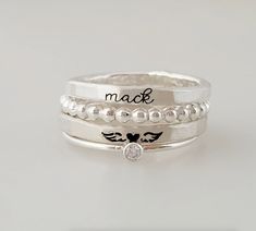 This elegant memorial ring set is the perfect gift to honor a loved one. Crafted of high-grade sterling silver and fine silver, the angel wing name ring is a timeless and beautiful memento. Capture a name or special date to memorialize a loved one forever. Ring set includes four total rings: one name ring, one angel wing ring, a beaded ring, and a clear cz ring. Choose between the listed fonts and three metal options: silver or 14K yellow gold filled. Gold-filled is a waterproof amazing alternat Elegant Silver Customizable Stackable Rings, Elegant Customizable Silver Stackable Rings, White Sterling Silver Ring With Engraving Option, Customizable Sterling Silver Engraved Ring, Personalized White Sterling Silver Engraved Ring, Custom Name White Sterling Silver Rings, Sterling Silver Memorial Ring With Birthstone, White Sterling Silver Personalized Stackable Rings, Anniversary Sterling Silver Stackable Rings With Engraving Option