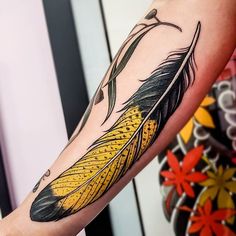 a woman's arm with a yellow and black feather tattoo on her left arm