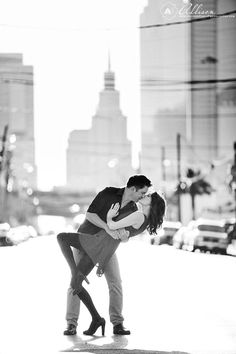 a man and woman kissing in the middle of a city street with tall buildings behind them