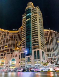 a very tall building sitting in front of some other buildings at night with lights on