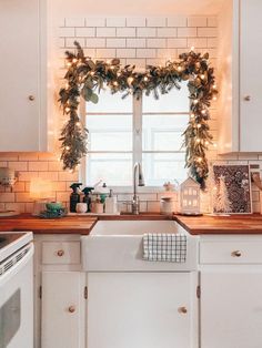 a kitchen decorated for christmas with garland and lights on the window sill above the sink