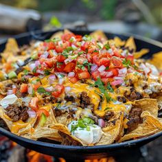 nachos with meat, cheese and tomatoes on top are served over an open fire