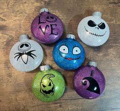 six ornaments with faces painted on them sitting on a wooden table, including one for halloween and the other for jack - o - lantern