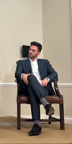 a man in a suit and tie sitting on a chair next to another man with his feet crossed