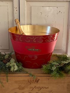 a large red and gold bucket sitting on top of a wooden box next to pine cones