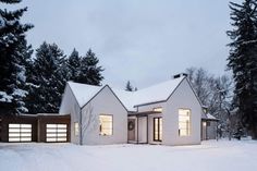 a white house in the snow with two garages on each side and trees behind it