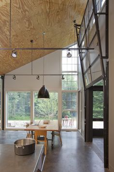 an open kitchen and dining room area in a house with wood ceilinging, large windows, and steel railings