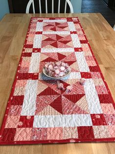 a table with a red and white quilt on top of it next to a bowl of flowers