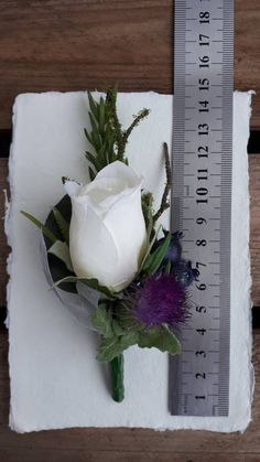 a white rose and purple flowers are on a piece of paper with a measuring tape