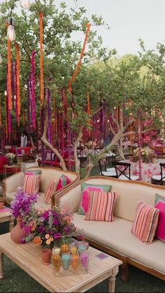 an outdoor seating area with pink and orange pillows, white couches, and trees