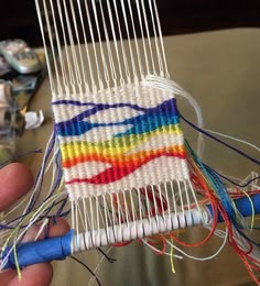 someone is holding up a colorful piece of yarn with scissors and thread on the table