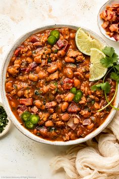 a white bowl filled with chili and beans next to a lime slice on the side