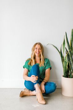 a woman sitting on the floor next to a potted plant and holding a pillow