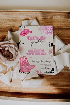 a pink and white wedding card on top of some torn up pieces of paper next to a flower