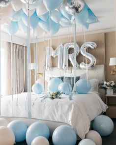 blue and white balloons are hanging from the ceiling above a bed in a room with a large mirror