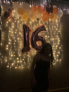 a woman standing in front of a wall with balloons and lights hanging from it's sides