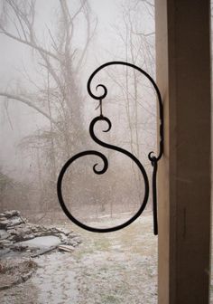 an iron letter s hanging on the side of a building in the snow with trees behind it