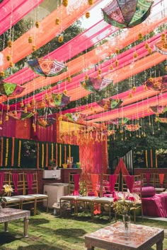 an outdoor wedding venue with pink and yellow decorations on the ceiling, hanging from strings