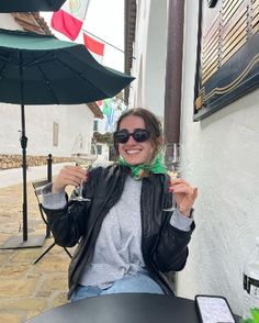 a woman sitting at a table with a glass of wine and an umbrella in the background