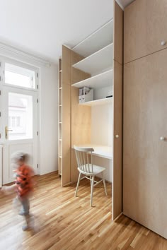 a small child is walking in the room with wooden floors and shelving unit behind him