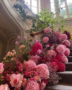 pink and red flowers sitting on the steps in front of an ornate staircase with arched windows