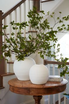 two white vases sitting on top of a wooden table next to a stair case