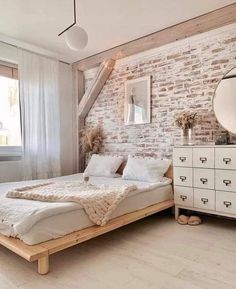 a bedroom with brick wall and white bedding, wooden dressers and large mirror