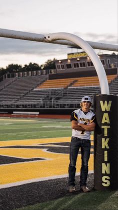 a man standing in front of a sign on the side of a football field with his arms crossed