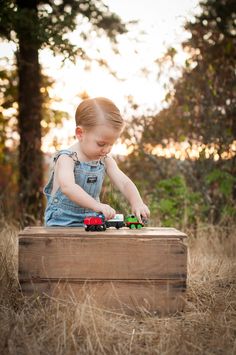 a toddler playing with toy trucks in a field at sunset or sunrise hour,