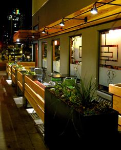 a row of benches sitting next to each other on a sidewalk at night with buildings in the background