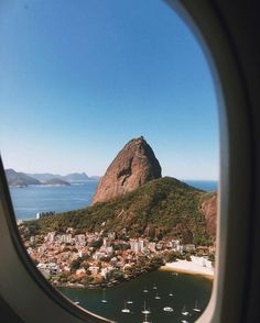 an airplane window looking out at the city and mountains in the distance with sailboats on the water