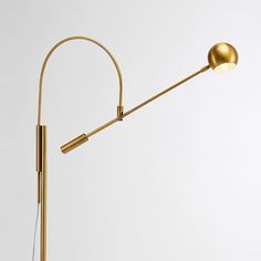 a gold colored floor lamp on a white background with a round light bulb attached to it