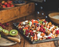 a waffle topped with berries, kiwis and strawberries on top of a wooden table