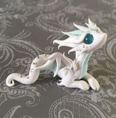 a white dragon figurine sitting on top of a gray tablecloth with paisley designs