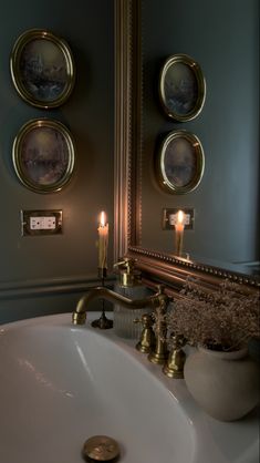 a bathroom sink with three pictures on the wall above it and candles in front of it