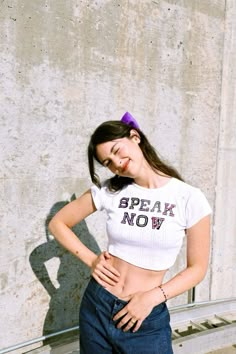 a woman standing in front of a concrete wall with her hands on her hips and looking at the camera