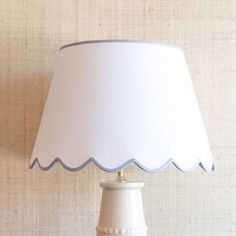 a white lamp with a blue shade on the top and bottom, against a beige wall