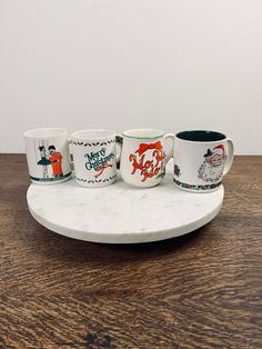 five coffee mugs sitting on top of a marble tray with merry christmas designs around them