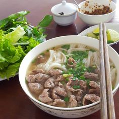 a bowl of soup with chopsticks next to it and another bowl of salad in the background